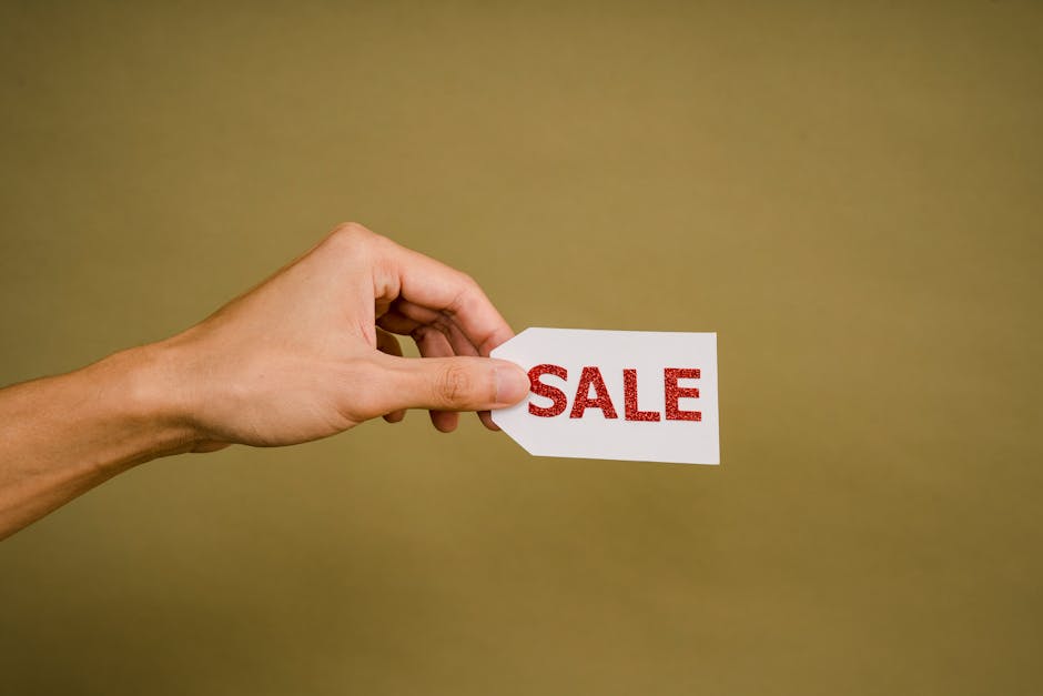 A hand holding a 'SALE' tag on a brown background, perfect for retail promotion.